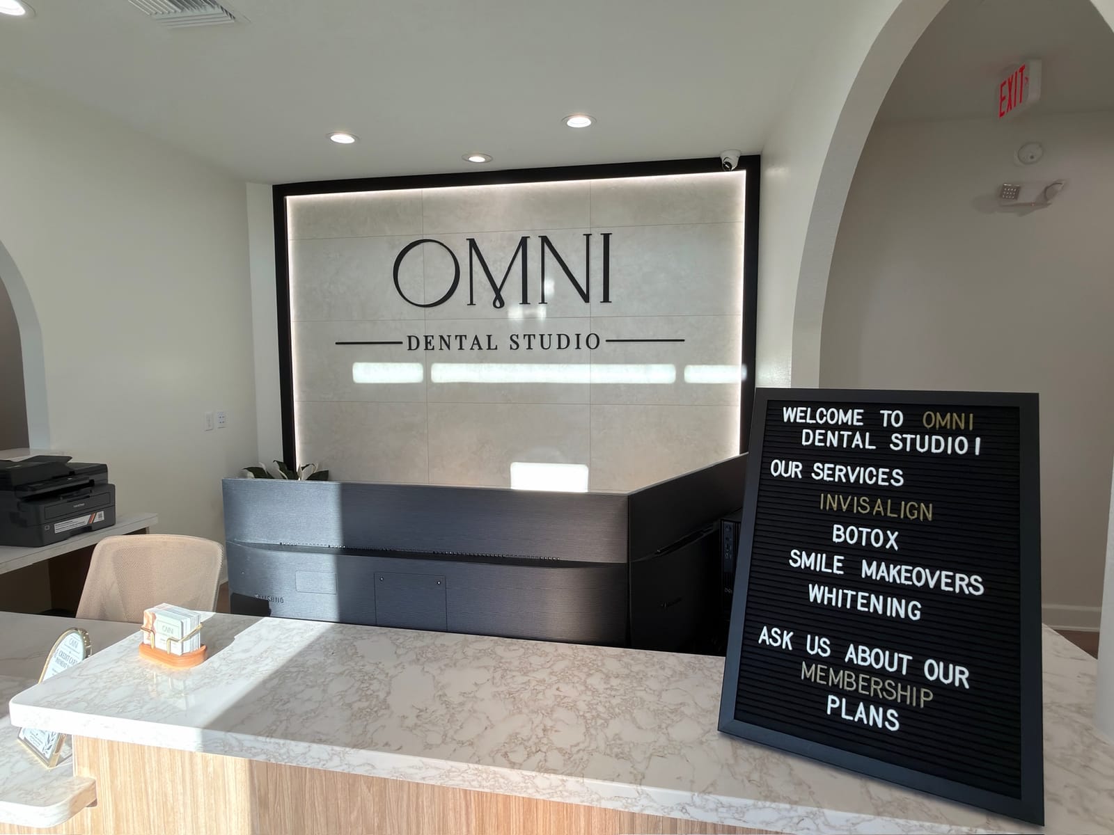 The Omni Dental Studio front desk with the illuminated OMNI logo wall and a welcome letter board
